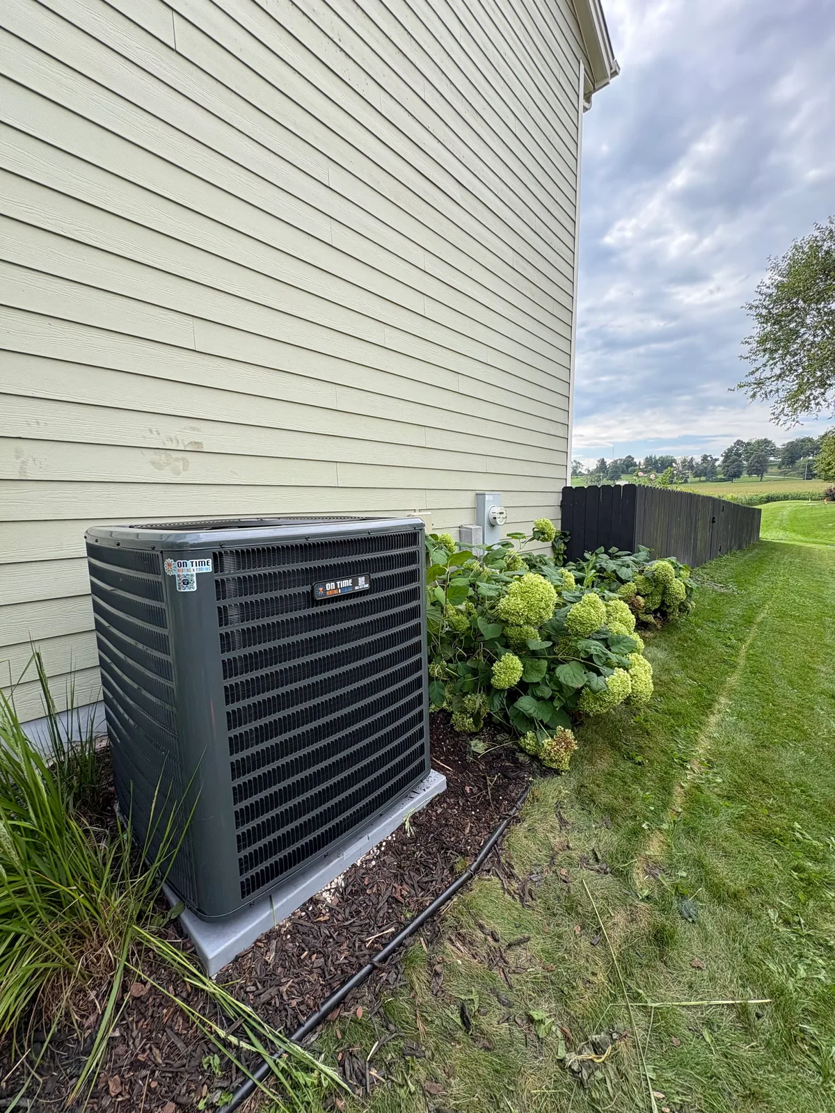 On Time Heating & Cooling air conditioner installed beside a home with hydrangeas